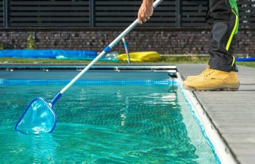 worker cleaning pool with a skimmer